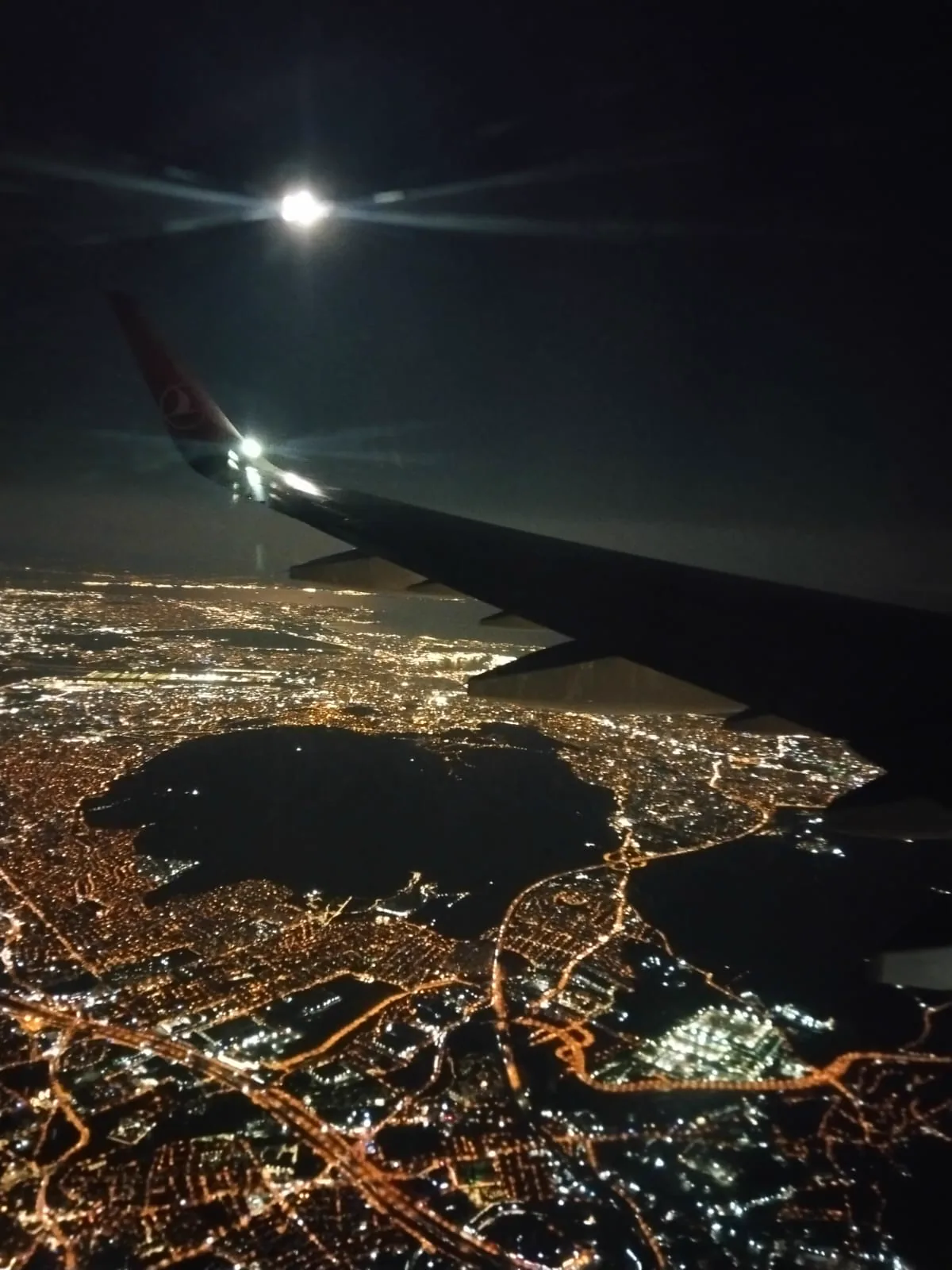 Uçak kanadının altında gece ışıklarıyla görünen şehir