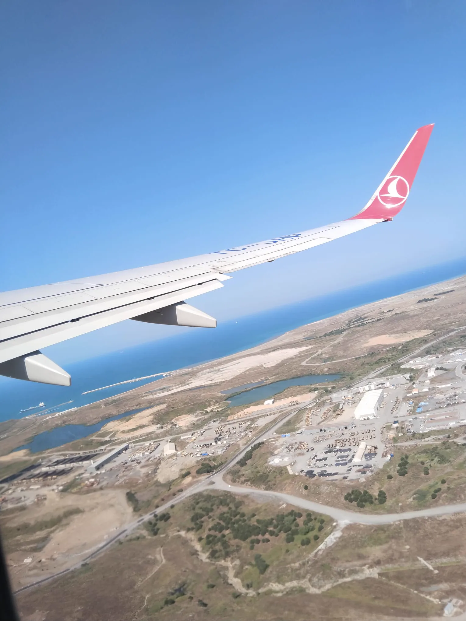 Uçak kanadı, mavi gökyüzü ve aşağıdaki kıyı manzarası